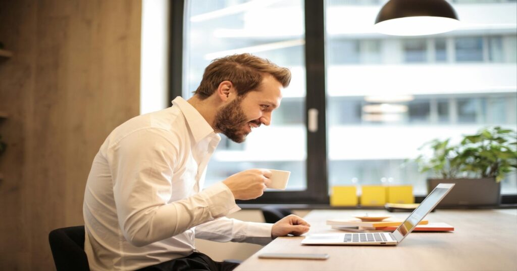 A Man Smiling at the Laptop and taking tea | Make Money from Virtual Assistant Jobs